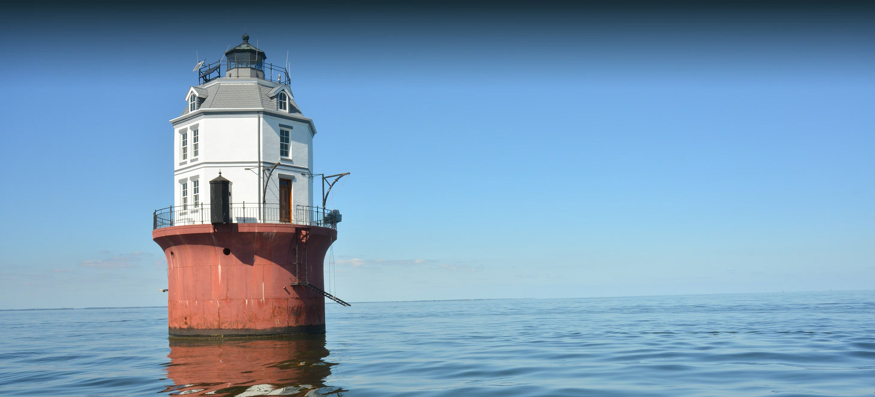a sole lighthouse sitting in a calm ocean on a sunny day. there is no visible land—the lighthouse comes directly out of the water and is about 3 stories tall.