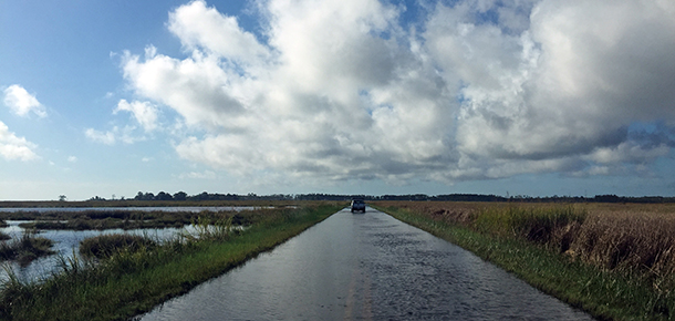 Flooded road with a car driving down it.