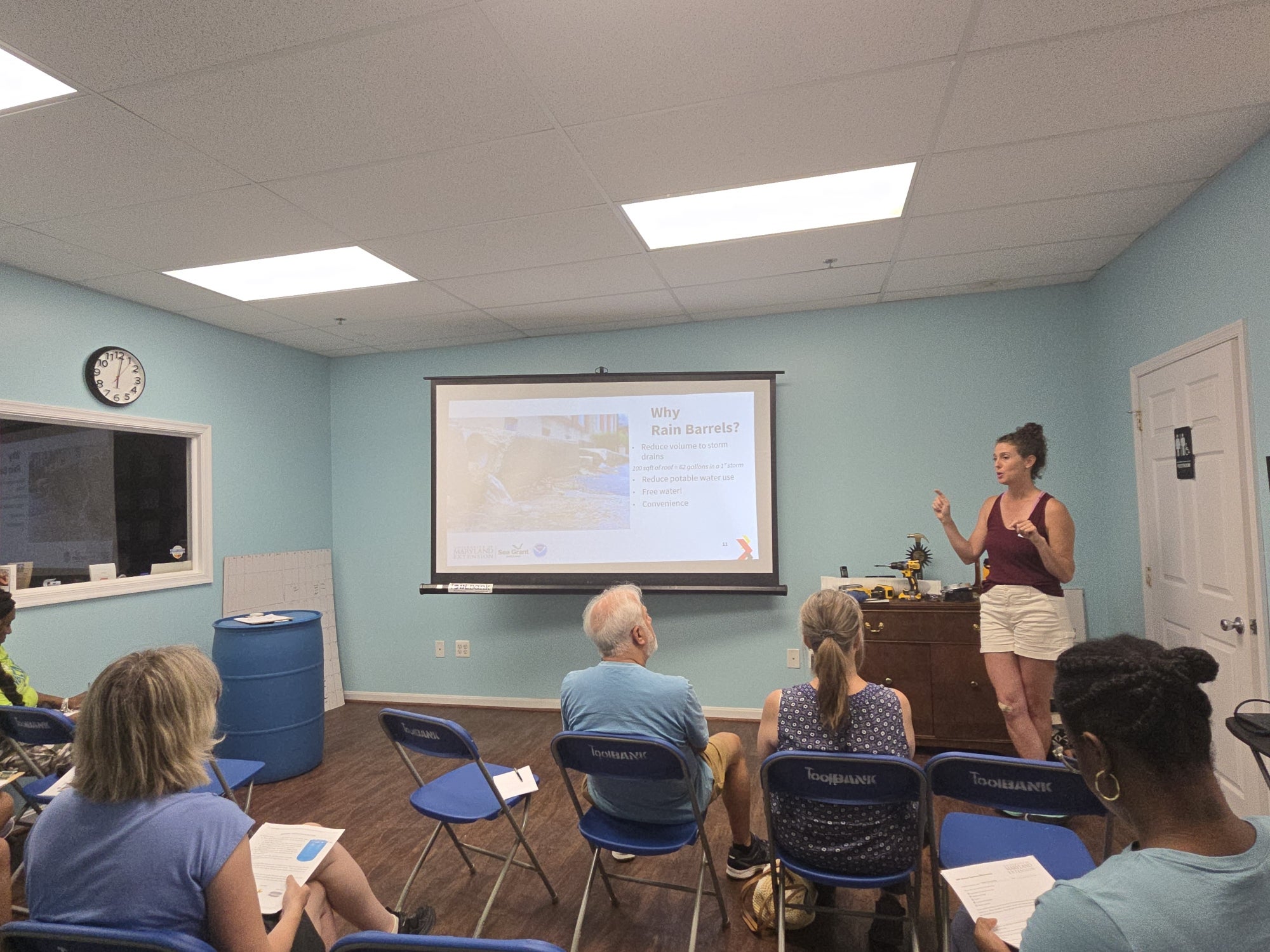 A woman speaks to a small room of people about rain barrels