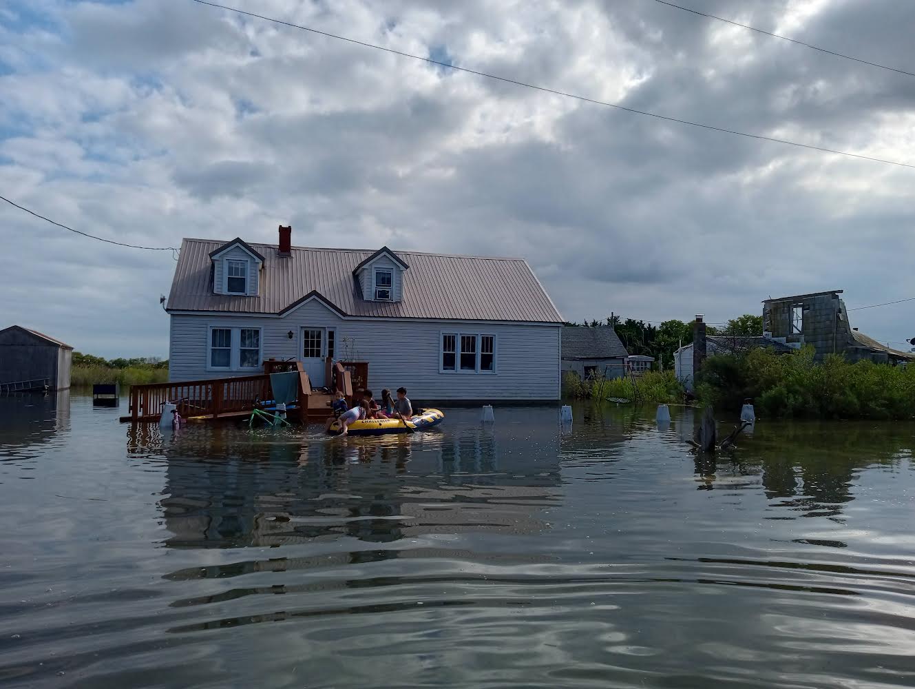 Several children row an inflatable raft through floodwaters that rise to the foundations of houses on Smith Island