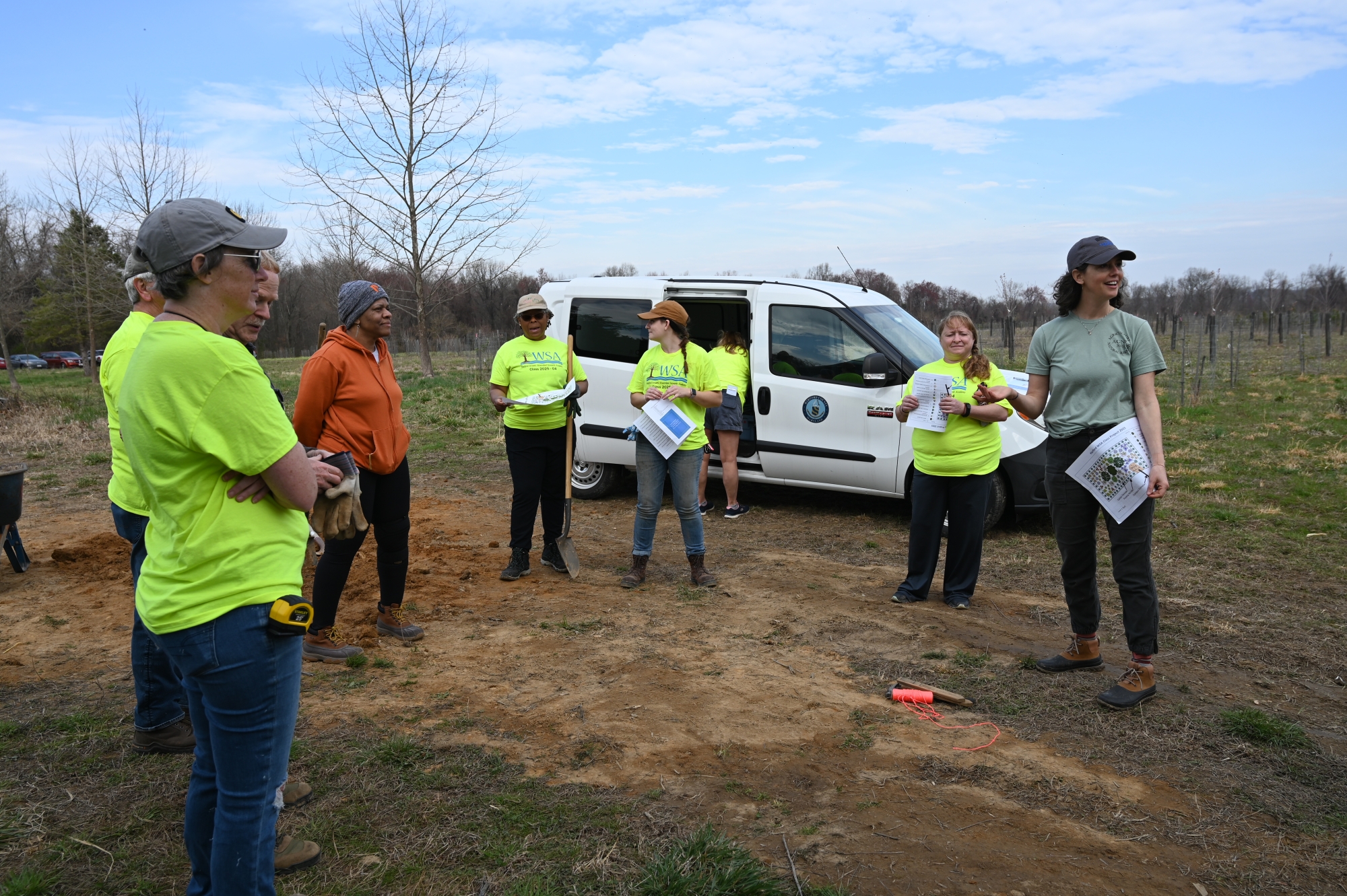 Volunteers gather in a circle in a field near a car.