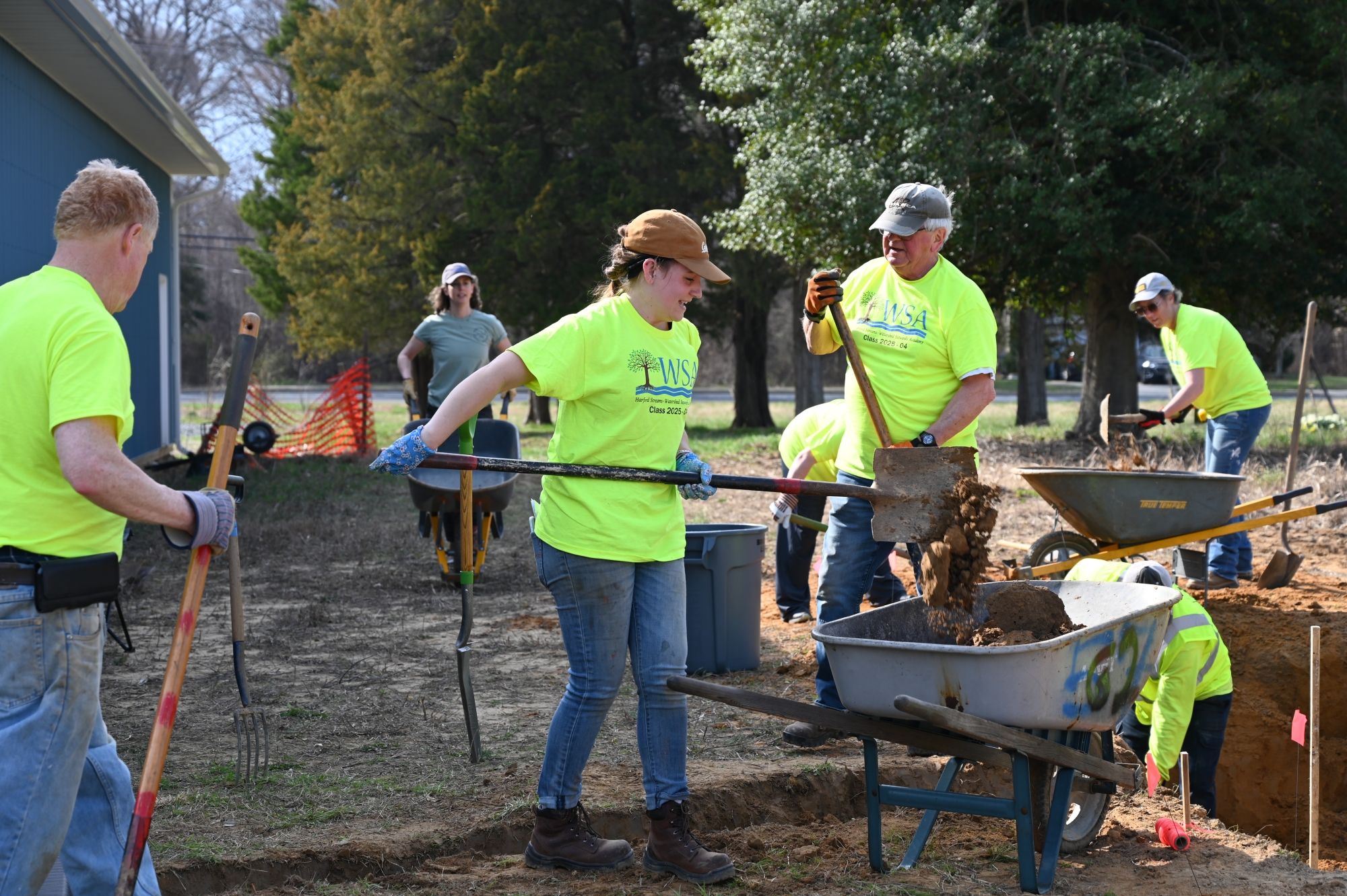 Several volunteers shovel dirt into wheelbarrows.
