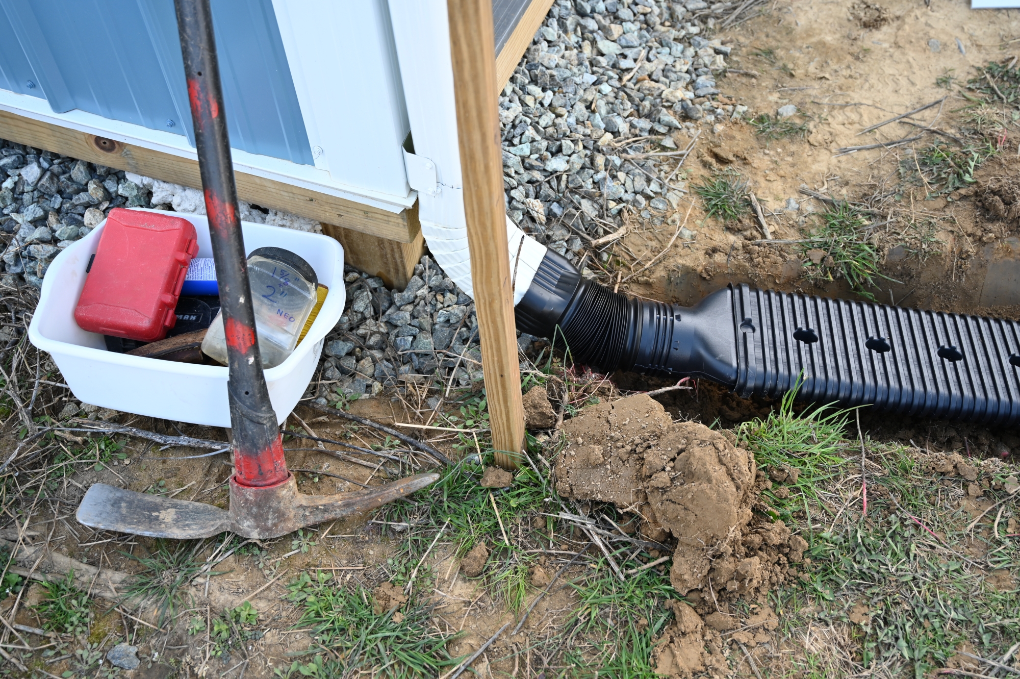 A pickaxe rests next to a downspout at the corner of a barn.