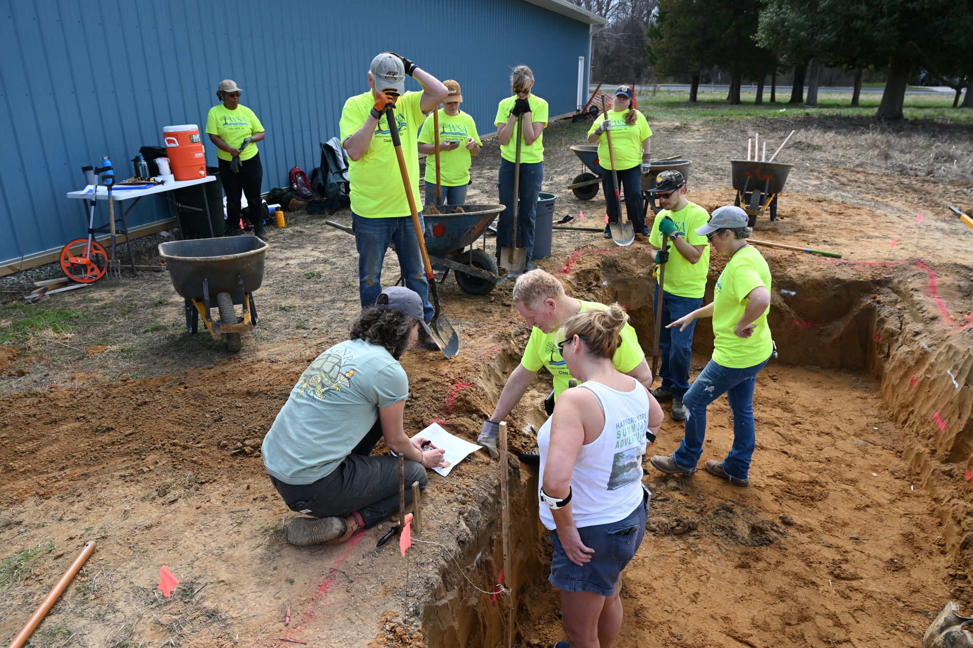 Volunteers near a freshly dug hole gather around a piece of paper for discussion of the plan.