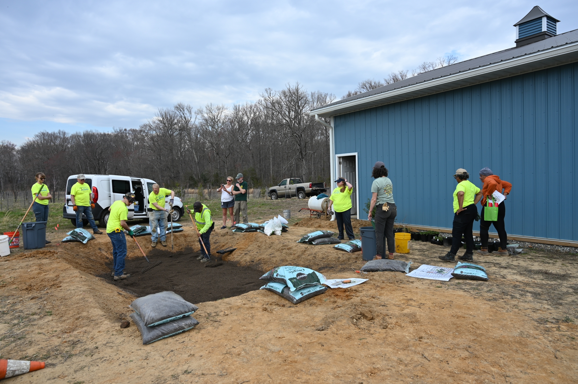 Two people rake dirt in a hole while several others look on.