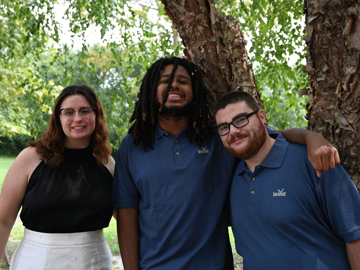 Three students pose together next to a tree