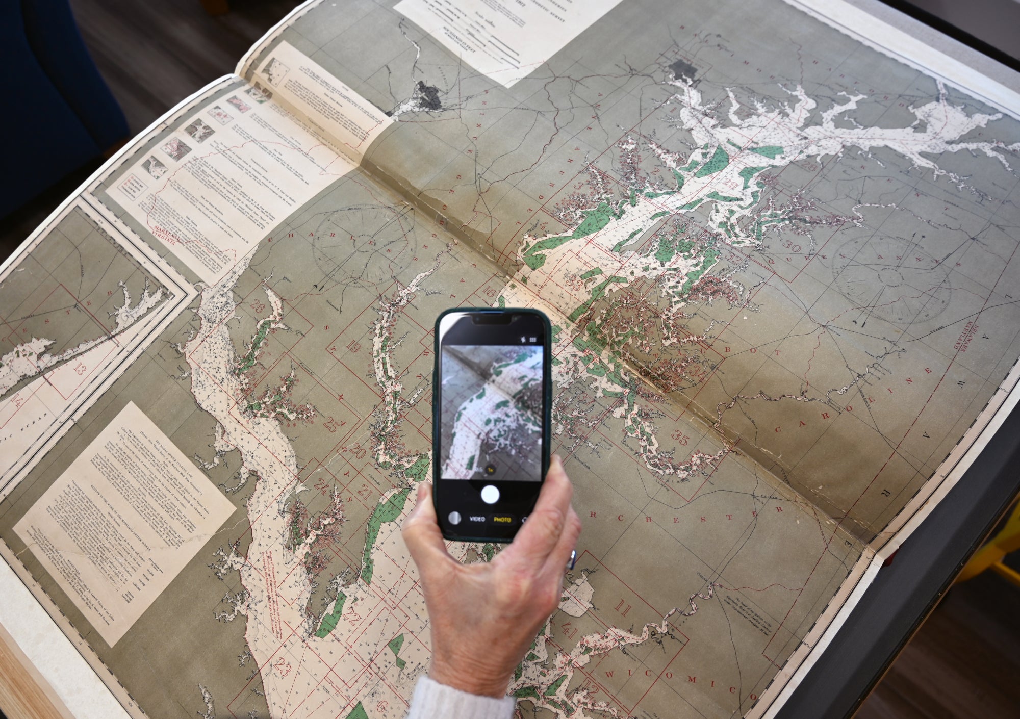 The Yates charts book is opened to a full-Bay chart and a hand holds a phone above the chart to give an idea of the book's large size