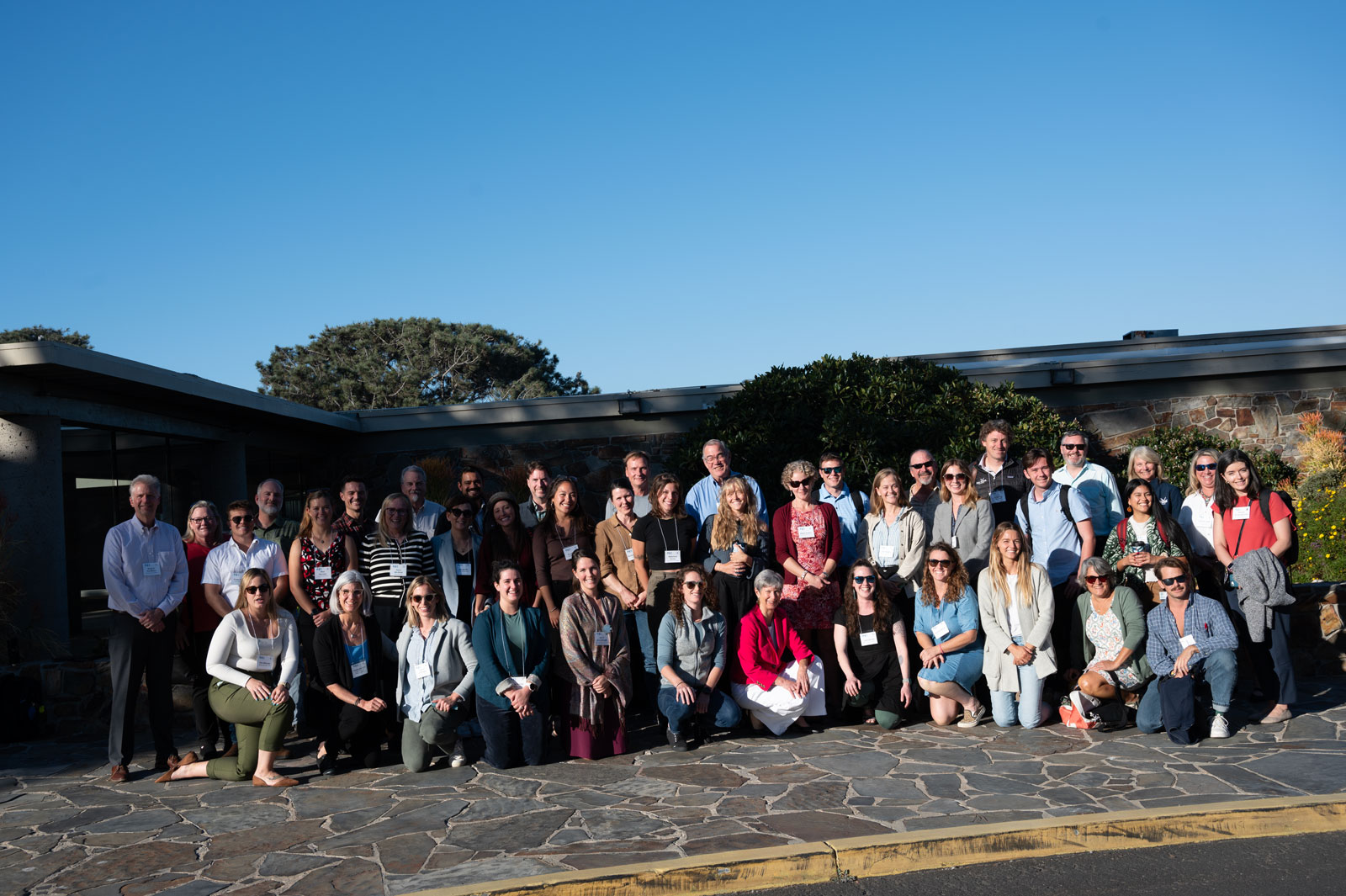 A large group of people pose together on a flagstone pathway outside a building