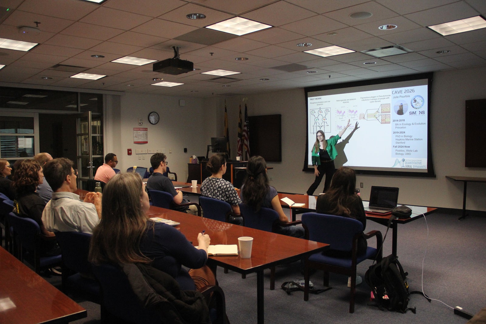 A researcher points at slides on a projector screen during a presentation to a room of other researchers