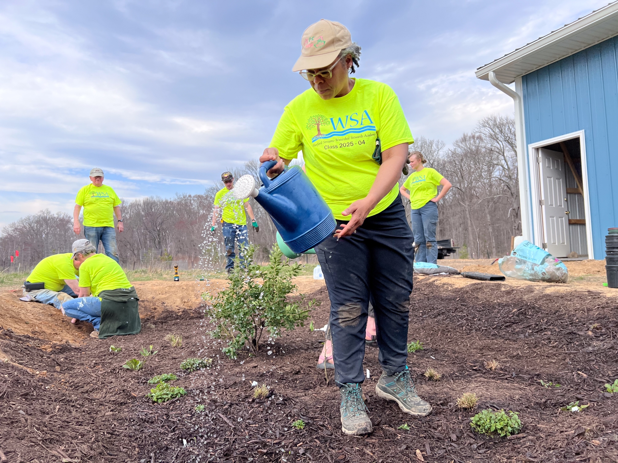 A woman waters plants while other volunteers pat down the edges of the garden.