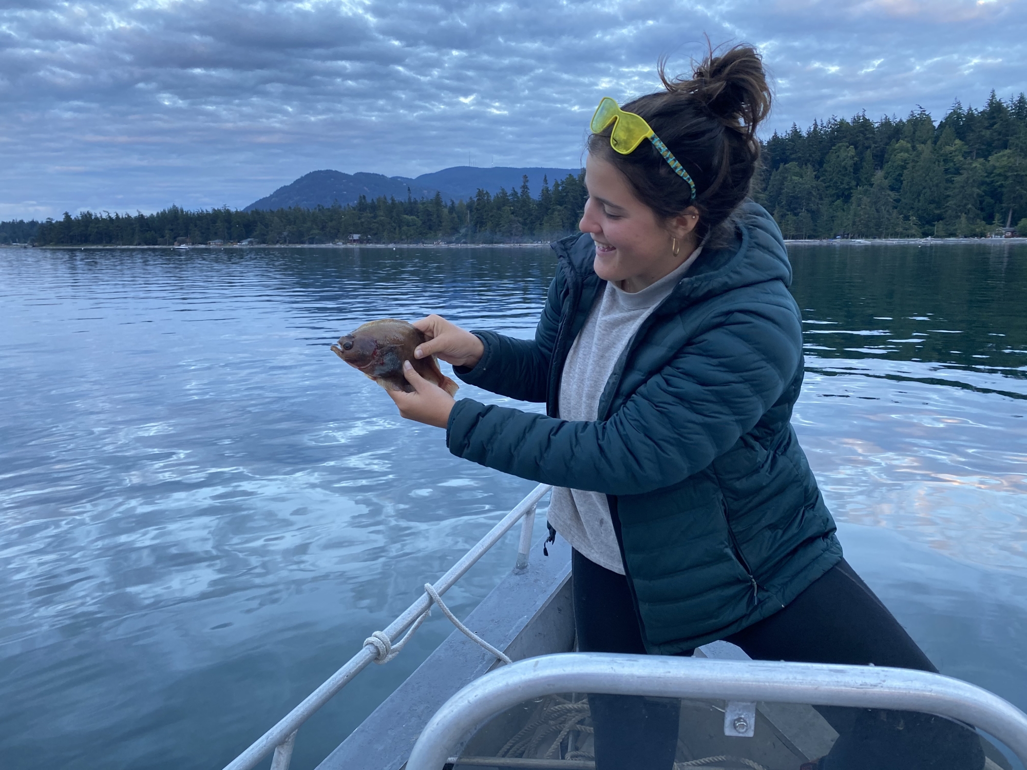 A woman on a boat on a lake holds a small fish