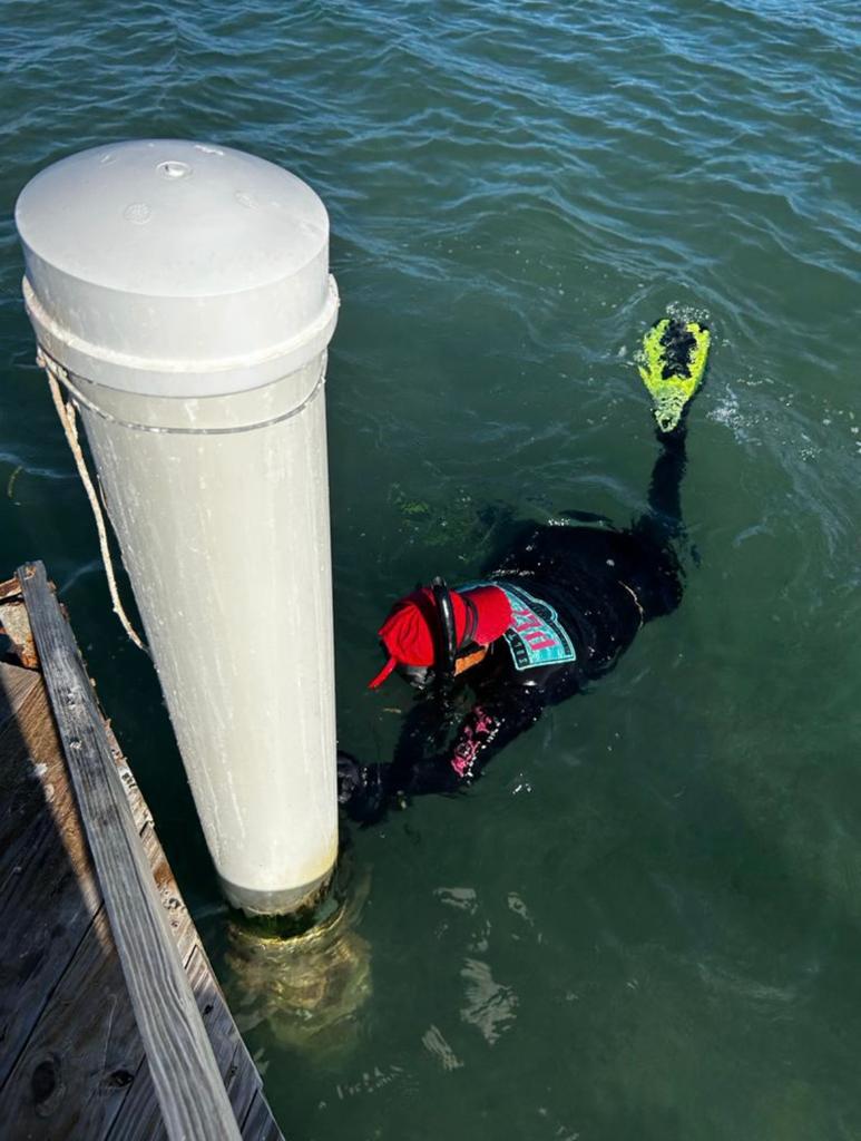 Mairim swims in the water in snorkeling gear and cleans a large pvc pipe