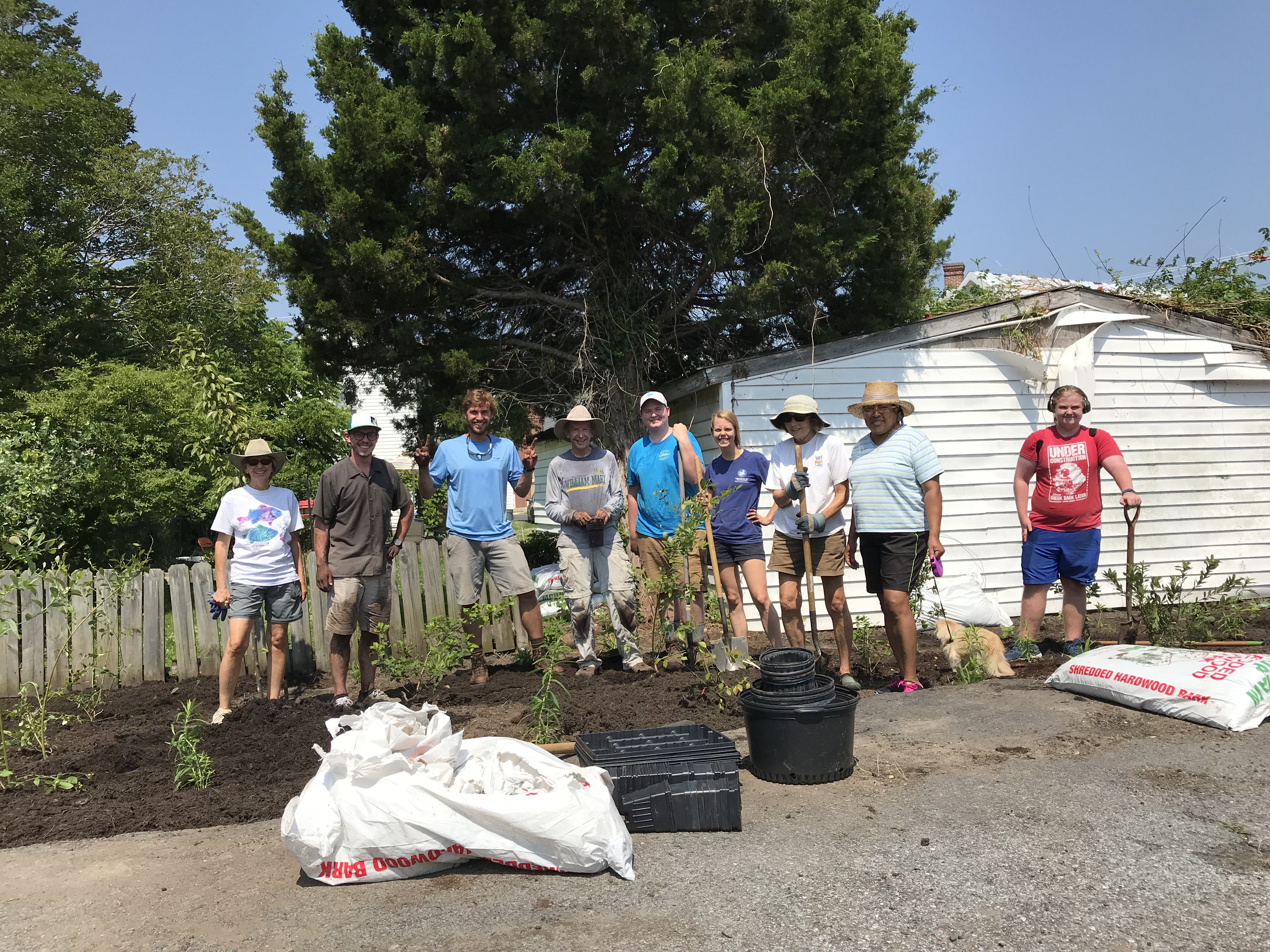 9 people stand among newly planted native plants at the edge of a parking lot