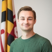 Man wearing green shirt in front of Maryland state flag, smiling.