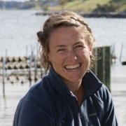 Woman smiling wearing dark blue jacket in front of water.