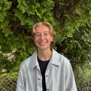 Delaney Mezan smiling with a grey button up shirt, and trees in the background