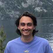 Michael Kalinowski smiling wearing purple shirt, the background is of mountains and a body of water.
