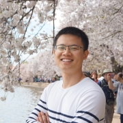 Man wearing white and black striped shirt, smiling and standing in front of cherry blossoms.