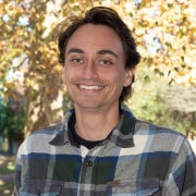 Michael Kalinowski smiling with a plaid black shirt, and trees in the background