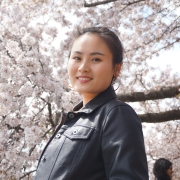 Woman smiling wearing dark colored jacket in front of cherry blossoms.