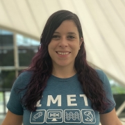 Headshot of woman smiling wearing a green IMET t-shirt in front of light background