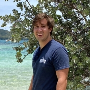 Matt Stefanak standing in front of a tree and water body, wearing navy blue t-shirt.