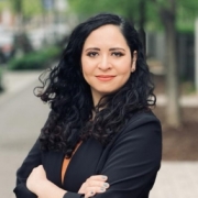 Woman wearing black blazer, smiling and standing in front of a street.