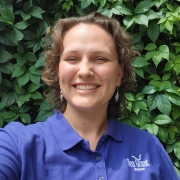 Headshot of Hannah wearing a blue MDSG polo and standing in front of a plant wall. 