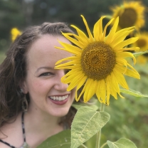 A woman smiling for a selfie next to a sunflower