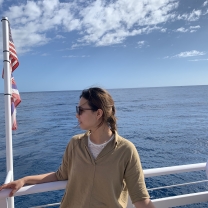 Ju-Ching Huang stands next to a metal railing, looking into the distance. A body of water is in the background.