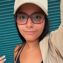 A portrait of Mairim M. Villafañe-Vicente wearing a tank top, jacket, glasses, and a baseball hat