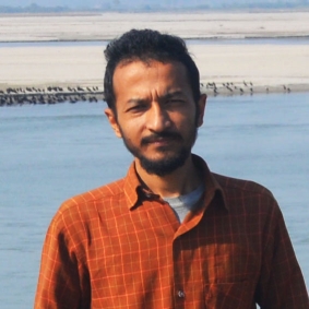 Man wearing burnt orange colored collar shirt standing infront of water.