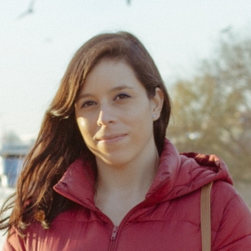 Closeup of woman wearing a red jacket and smiling in the sun.
