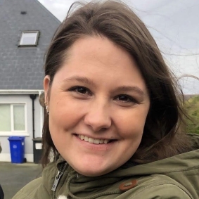 Brunette woman smiling wearing olive green jacket .