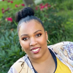 Black woman smiling in front of red flowers and greenery.