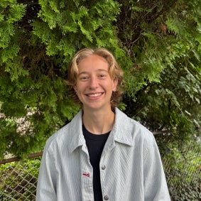 Delaney Mezan smiling with a grey button up shirt, and trees in the background