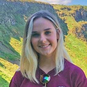 Blonde woman with maroon shirt in front of green background.