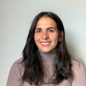 Headshot of woman smiling wearing light purple turtleneck in front of grey background.