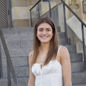 Grace O'Hara smiling standing infront of outdoor stairs and wearing a white shirt.