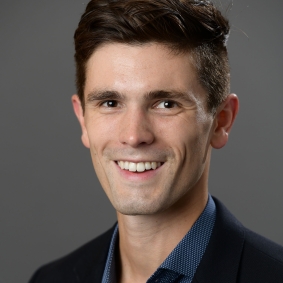 Headshot of man smiling, wearing blue collared shirt and black suit jacket.