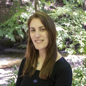 White woman wearing black shirt in front of greenery.