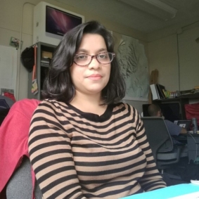 Khurshid Jahan with black hair and a horizontally striped shirt, siting at a table.