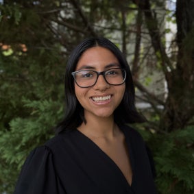 Headshot of a woman smiling wearing a black blouse, with trees in the background
