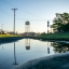 Water pools on a gravel road between a parking lot and building on a sunny day. An old water tower and power lines are in the distance, reflected in the pool of standing water.