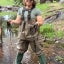 Julia Devine stands in a shallow creek wearing waders and holding long, stringy mats of algae
