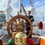 Abdulmajid Alrefaie stands behind the large wooden wheel of a ship