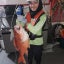 Aiman Raza wears a vest and hard hat and holds a red snapper aboard a research vessel