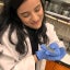 A woman in lab coat and gloves holding a small blue crab