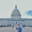 A young man in a suit stands in front of the US Capitol building