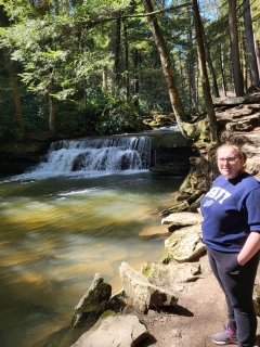 A young woman stands on rocks near a small waterfall in a forest